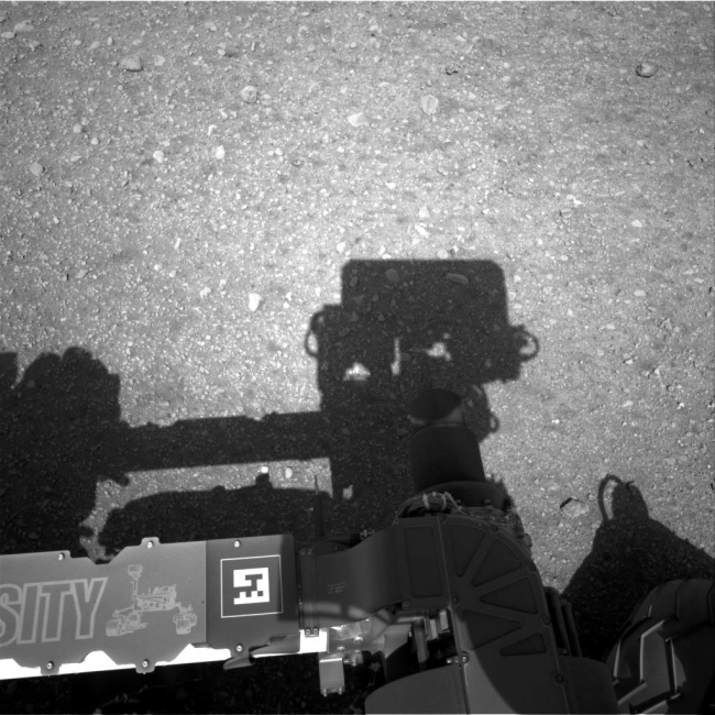 Curiosity Looks Away from the Sun,  This is the first image taken by the Navigation cameras on NASA's Curiosity rover. It shows the shadow of the rover's now-upright mast in the center, and th...